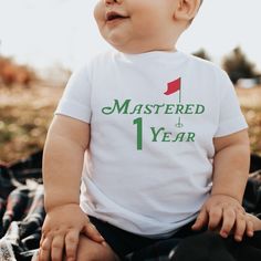 a baby sitting on the ground wearing a tee shirt that says, mastered 1 year