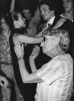 black and white photograph of an older woman dancing with a group of people in the background