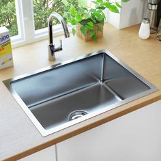 a stainless steel kitchen sink on a wooden countertop next to a window with potted plants