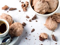 two white bowls filled with chocolate ice cream next to spoons and cups of coffee