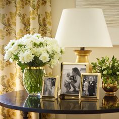 a table topped with pictures and flowers on top of a glass table next to a lamp