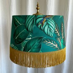 a green lamp shade with gold fringes and tropical leaves on the lampshade