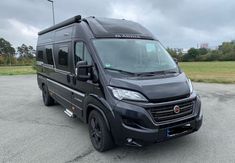 a black van parked in a parking lot next to some grass and trees on a cloudy day