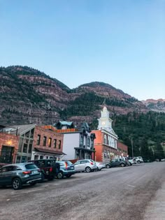 cars parked on the side of a road in front of buildings with mountains in the background