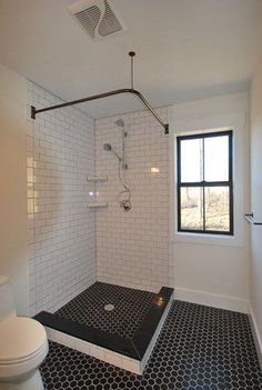 a black and white tiled bathroom with a shower, toilet and window in the corner