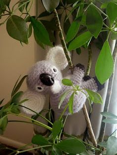 a stuffed koala bear hanging from a tree branch in front of a window with green leaves