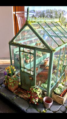 a small green house sitting on top of a stone slab next to potted plants