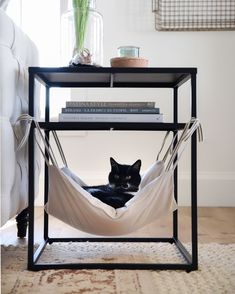 a black and white cat laying in a hammock under a table with books on it