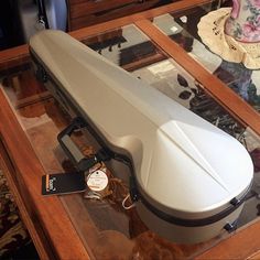 a white guitar case sitting on top of a glass table next to a clock and hat