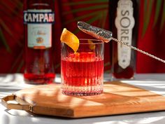 a wooden cutting board topped with a glass filled with red liquid and a lemon wedge