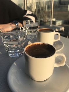 three cups of coffee sit on a table with water in front of them and one cup is filled with liquid