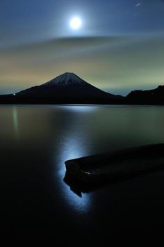 the moon shines brightly in the night sky over a lake with a mountain in the background