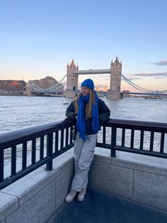 a woman standing on the side of a bridge next to a body of water with a bridge in the background