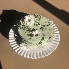 a green cake sitting on top of a white plate covered in daisies and leaves