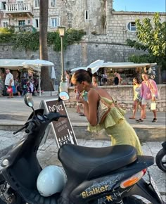 a woman standing next to a scooter on the street