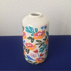 a white vase sitting on top of a blue table with flowers painted on the side