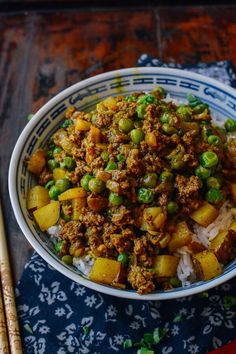 a bowl filled with rice and meat on top of a table next to chopsticks