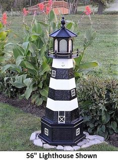 a black and white light house sitting on top of a lush green field next to flowers