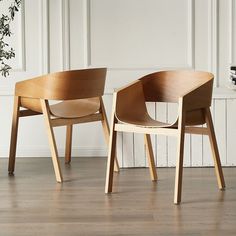 two wooden chairs sitting next to each other on top of a hard wood floor in front of a white wall