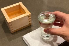 a person holding a glass in front of a small wooden box on a counter top