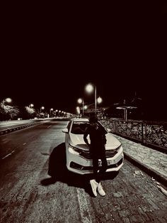 a person standing next to a parked car on the side of a road at night