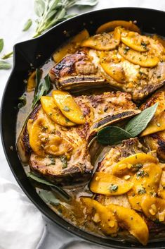 a skillet filled with meat and vegetables on top of a white cloth next to a green leaf