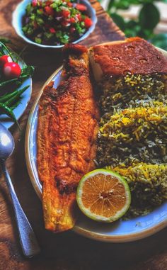 a plate with fish, rice and other food on it next to a bowl of salad