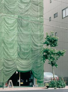 a large green curtain covering a building next to a tree on the side of the road