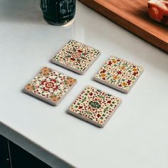 four coasters on a counter with fruit and bread in the background