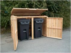 two black trash cans are in the back of a wooden storage shed with doors open