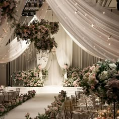 an elegant wedding setup with white draping and pink flowers on the ceiling, along with floral arrangements