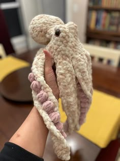 a hand holding an octopus stuffed animal in it's palm, on a table