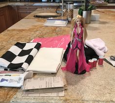 a barbie doll sitting on top of a counter next to some papers and other items