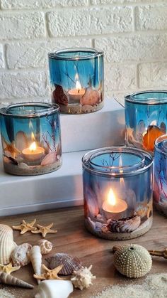 four glass candles with seashells in them on a table next to shells and starfish