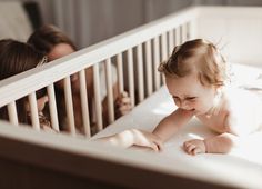 a baby laying in a crib next to an adult and another child on the bed