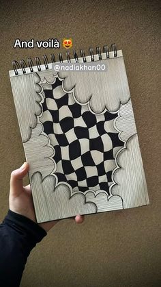 a hand holding up a spiral notebook with black and white checkered paper on it