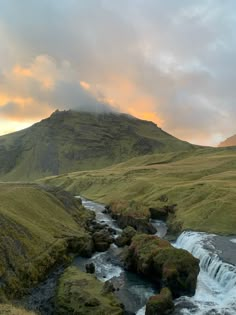 a river running through a lush green hillside next to a mountain covered in grass and trees