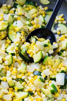 corn and zucchini are being cooked in a skillet with a black spoon