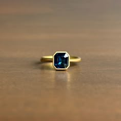 a gold ring with a blue stone on it sitting on a wooden table next to a brown surface