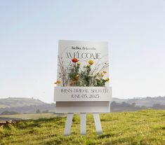 a sign in the middle of a field with flowers on it that reads, welcome