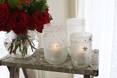 red roses and candles sit in glass vases on a wooden table next to a window