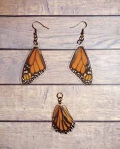 three pieces of jewelry sitting on top of a wooden table with one butterfly hanging from it's ear