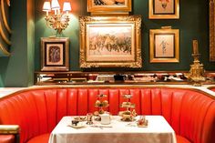 a restaurant with red booths and gold framed pictures on the wall, along with white tablecloths