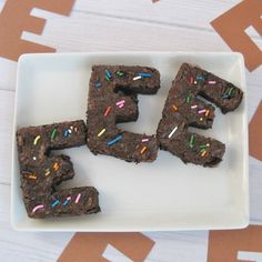 four brownies with sprinkles and the letter e spelled out on a plate