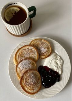 some powdered sugar and jelly are on a plate next to a cup of coffee