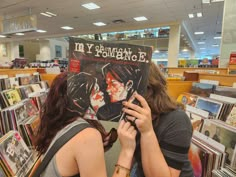 two women are looking at an album in a bookstore aisle with books on the shelves