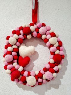 a red and white wreath hanging on the wall with a heart shaped decoration attached to it