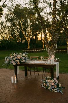 a table with flowers and candles on it in the middle of a park at sunset