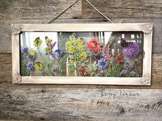 a wooden frame with flowers on it hanging from a wall next to a sign that says,