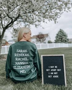 a woman sitting in the grass next to a sign